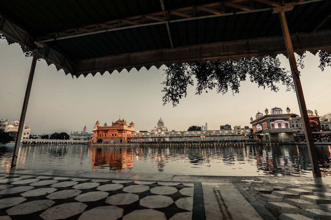 Sidewalk with roof near water with illuminated ancient buildings with fence against gray sky in city street in evening time